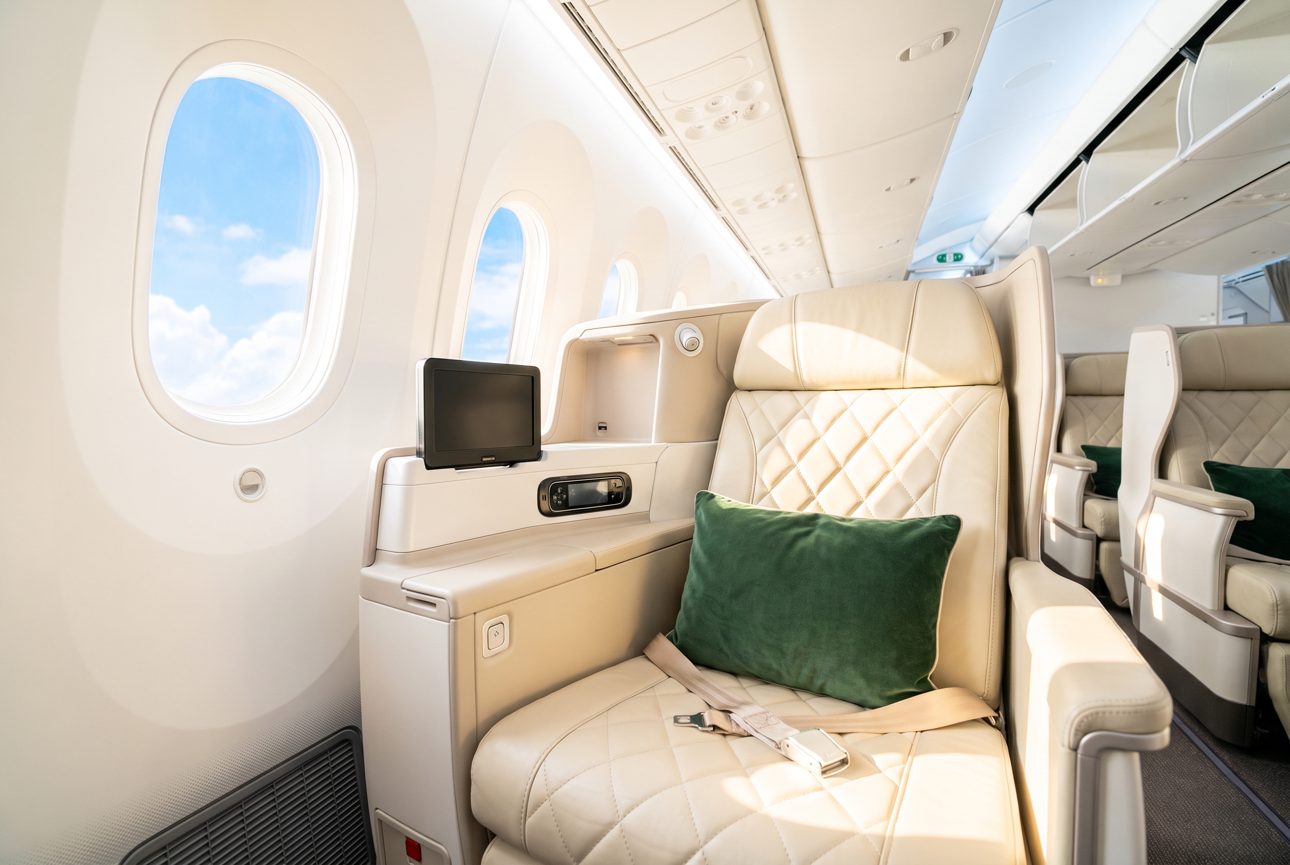 A modern first-class seat in cream leather with a green pillow